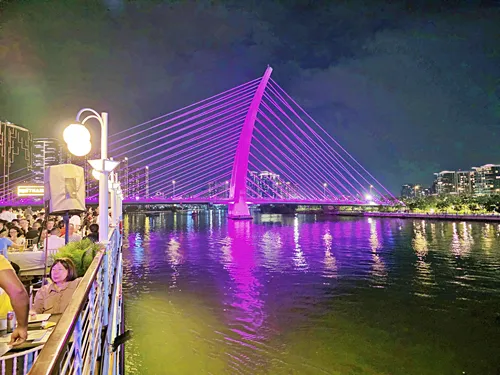 photo taken on the upper deck of a Saigon River Dinner Cruise in Vietnam. The colorfully illuminated skyline and bridge at night can be seen in the photo