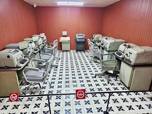 photo of a room in the bunker Reunification Palace in Ho Chin Minh City, Vietnam, showing many desks with many desks, typewriters, and a printer